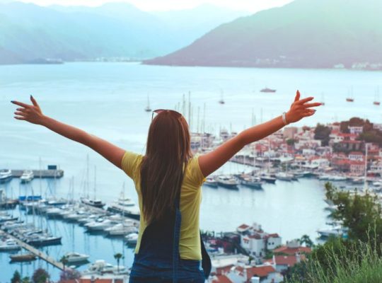 Woman Raising Her Hands Facing Cityscape Near Body of Water